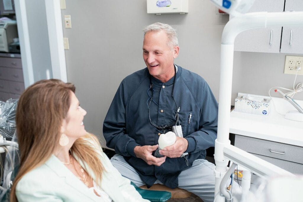 Dentist discussing dental care with a female patient while holding a dental model in a modern clinic.